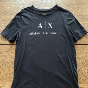 Svart t-shirt från Armani Exchange - Säljer en svart t-shirt från Armani Exchange med vit logotyptryck på bröstet. Klassisk rund halsringning och normal passform. Perfekt för dig som gillar stilrena plagg. Storlek L, sparsamt använd. 