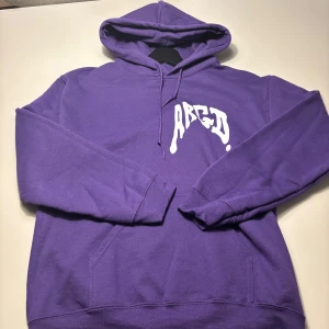 Lila hoodie från ARGD - Säljer en lila hoodie från ARGD med vit tryckt logga på bröstet. Tröjan har huva med dragsko och en stor magficka. Perfekt för dig som gillar skate och streetwear och vill ha något bekvämt och snyggt. Storlek S men oversize, nypris ca 1000 kr. ARGD donerar en del av intäkterna till överlevande av sexuella övergrepp !! aldrig använd
