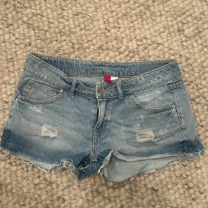 Blå jeansshorts med slitningar - Snygga blå låg midjade jeansshorts med slitna detaljer och fransig kant. 