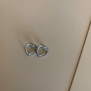 Hjärtformade örhängen - Säljer ett par örhängen i form av hjärtan i silverfärg. Perfekta för att ge en söt touch till din outfit. Passar både till vardag och speciella tillfällen. Skriv om du har frågor o läs gärna min bio innan du köper🫶🏻🫶🏻