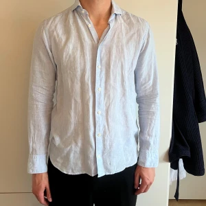 Ljusblå linneskjorta från Eton - Säljer en stilren ljusblå skjorta i linne med klassisk krage och vita knappar. Skjortan har lång ärm och en avslappnad passform.