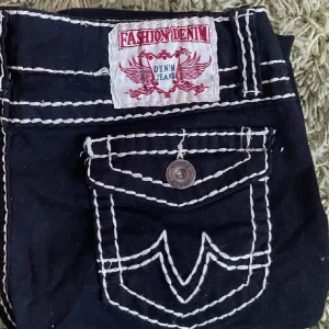 Svarta jeans  - Svarta jeansbyxor från Fashion Denim med tydliga vita kontrastsömmar och dekorativa fickor med knappdetalj bak. Snygg och unik design som sticker ut. Storlek 44 men passar mindre!💗