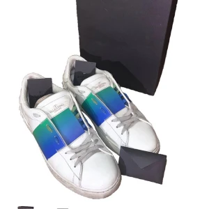 Valentino skor - Säljer ett par vita Valentino sneakers med en bred blågrön rand över mitten. Skorna har snörning och rund tå, samt diskret Valentino-logga på plösen. Klassisk och stilren design med en färgklick som sticker ut. Rätt slita skulle säga att den är 6/10 men håller som dem ska.(äkta) nyligen redgjorda så bättre än på bild