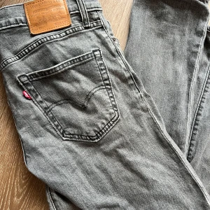 Gråa Levis 511 jeans - Säljer ett par klassiska gråa Levis 511 jeans femficksmodell. Byxorna har den ikoniska Levis-lappen bak i midjan och röd Levis-tagg på bakfickan. Perfekta för en avslappnad och tidlös stil. L32