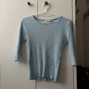 Ljusblå ribbad tröja från Hennes - Säljer en ljusblå ribbad tröja från super gamla H&M i storlek M (det var min mammas). Tröjan har trekvartsärm och rund halsringning. Perfekt för lager-på-lager och enkel att matcha med olika outfits. 
