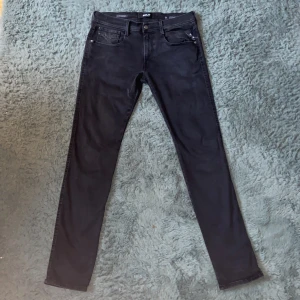 Replay Anbass Jeans  - Säljer ett par svarta jeansbyxor från Replay med klassisk femficksdesign och raka ben. Storlek 33/34. Byxorna har dragkedjegylf och diskreta detaljer, perfekt för en stilren look. Märkeslogga syns på fickan och bak på linningen.