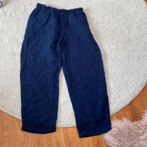 Marinblå linnebyxor från H&M - Säljer ett par mörkblå linnebyxor från H&M i storlek XS. Byxorna har resår i midjan med knytband och raka, lösa ben. Perfekta för en avslappnad och stilren look. På bilden ser de korta ut men de är inte så korta som de ser ut. 