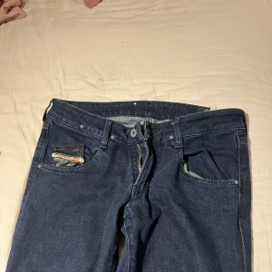  Lågmidjade bootcut jeans  - Säljer ett par mörkblå jeansbyxor från Diesel med bootcut-passform. Byxorna har detaljerade bakfickor med svarta skinnliknande kanter. Jag har sytt om dom till bootcut men tjvärr är dom för långa för mig som är 155 