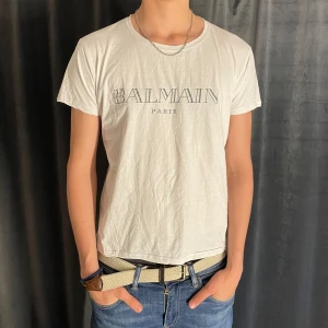 Vit t-shirt från Balmain Paris - Säljer en vit t-shirt från Balmain Paris med tryckt logga på bröstet. T-shirten har rund halsringning och korta ärmar. Perfekt för en varm sommardag. Storlek L men den är liten i storleken. Skick 7/10✅ Pris kan diskuteras vid snabb affär💸