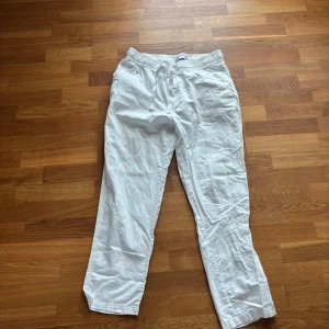 Vita linnebyxor med dragsko - Säljer ett par vita linnebyxor med avslappnad passform och dragsko i midjan. Byxorna har raka ben och resår i midjan för extra komfort. Perfekta för varma dagar och enkel stil.