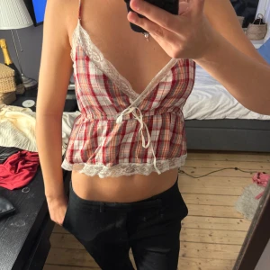 Rutig croppad linnetopp med spetsdetaljer - Säljer en söt röd- och vitrutig croppad linnetopp med smala axelband och spetsdetaljer längs v-ringningen och nederkanten. 