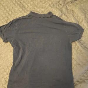 Mörkblå pikétröja från Polo Ralph Lauren - Säljer en klassisk mörkblå pikétröja från Polo Ralph Lauren i slim fit-modell. Tröjan har korta ärmar, krage och knappar framtill samt den ikoniska röda loggan broderad på bröstet. Perfekt för en stilren och avslappnad look. Fler bilder kontakta bara🌟
