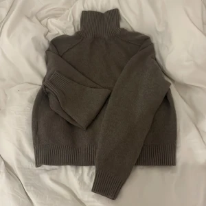 Grå stickad polotröja från H&M - Mysig grå stickad polotröja från H&M med ribbade muddar och hög krage. Perfekt för kyliga dagar och enkel att matcha med olika outfits. Klassisk modell med lång ärm och mjukt material.