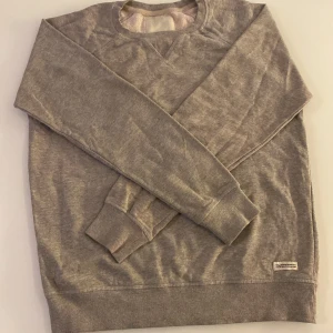 Grå sweatshirt från Weekday - En basic grå sweatshirt från Weekday med rund halsringning och ribbade muddar. Tröjan är mjuk på insidan och har en klassisk passform. Perfekt för en avslappnad stil.