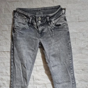 Grå jeansbyxor från LTB - Säljer ett par grå jeansbyxor från LTB med snygga detaljer som dubbla knappar och dragkedja vid fickan. Byxorna har normal passform och klassisk femficksdesign. Perfekta för dig som gillar en avslappnad men stilren look.
