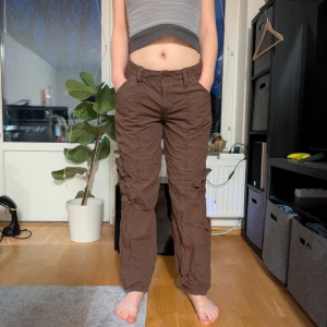 Bruna cargobyxor från BDG - Säljer ett par bruna cargobyxor från BDG Urban Outfitters. Byxorna har en avslappnad stil med elastisk midja och flera fickor för en praktisk look. Perfekta för en casual outfit.