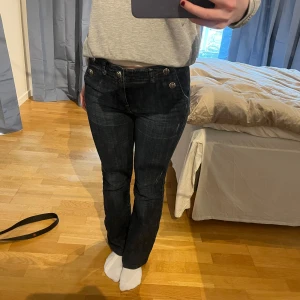 Mörkblå jeansbyxor med knappar från Easy Wear - Säljer ett par snygga bootcut-jeans i mörkblå från Easy Wear med flera silverfärgade knappar framtill som ger byxorna det där lilla extra. Klassiska bakfickor och en smickrande passform.  Stilren look som funkar till många outfits. 