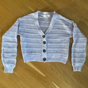 Ljuslila stickad kofta från H&M - Säljer en ljuslila stickad kofta från H&M med v-ringning och stora knappar framtill. Koftan är croppad och har lång ärm samt ett luftigt, hålstickat mönster. Perfekt för lager-på-lager och en söt detalj till din outfit!