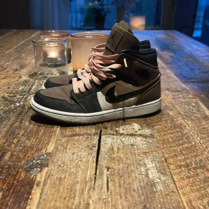 Nike Air Jordans 1 olive toe - Säljer ett par Nike Air Jordans med högt skaft i brunt, svart och vitt. Skorna har rosa snörning och en klassisk rund tå. Perfekta för dig som gillar streetwear och vill sticka ut med en unik färgkombo.