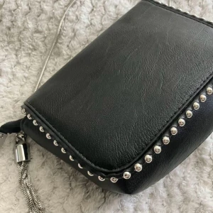 Svart axelväska med silverdetaljer - Svar axelväska i skinnimitation. Väskan är inprincip helt oanvänd med tanke på att den inte är min stil.