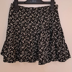 Blommig volangkjol från Lager 157 - Supersöt svart kortkjol med vita små blommor från Lager 157. Kjolen har volanger och en flowy passform som ger en skön vibe. Tillverkad i mjuk polyester med lite stretch för extra komfort. Storleken står inte men den passar mig som har xs-s 164-170