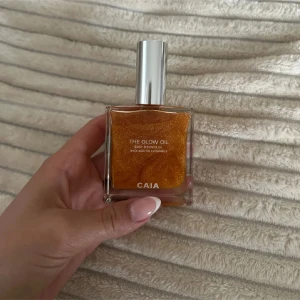 CAIA The Glow Oil shimmerolja - The Glow Oil från CAIA är en lyxig kroppsolja med guldigt skimmer. Oljan innehåller avokadoolja och vitamin E, perfekt för att ge huden en snygg glow. Kommer i en fyrkantig glasflaska med silvrig kork och har en varm, gyllene färg.