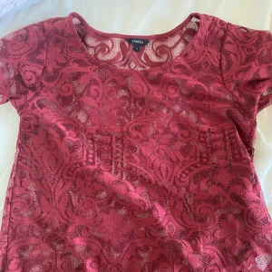 Vinröd spetsblus  - Supersnygg fest topp! En vinröd blus i spets med vackert mönster. Blusen har rund halsringning och korta ärmar med fina kanter. Perfekt för dig som vill sticka ut med en romantisk och trendig look. 