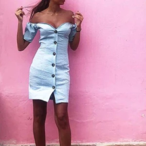 Ljusblå offshoulder kortklänning - Superfin ljusblå kortklänning med offshoulder och stora knappar framtill. Klänningen har en figurnära passform och korta ärmar, perfekt för varma dagar. Snygg och trendig look som passar till sneakers eller sandaler.