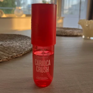 Sol de Janeiro Carioca Crush mist - Parfymmist från Sol de Janeiro i doften Carioca Crush. Flaskan är cylinderformad och genomskinligt röd med röd kork. Doften har fräscha noter av päron, rosa viol och vit cederträ. Perfekt för dig som gillar fruktiga och blommiga toner.