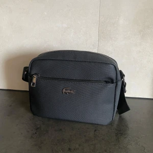 Lacoste bag - En svart Lacoste väska. Väskan har 4 olika fickor och stort utrymme. Skicket på väskan är 9/10. Sjukt bra skick och inga defekter. Priset kan diskuteras🙂
