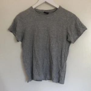Grå basic t-shirt i bomull - Enkel och stilren grå t-shirt från Basic i mjuk bomull. Modellen är klassisk med rund halsringning och korta ärmar. Perfekt för dig som gillar en clean och avslappnad look.