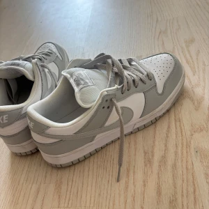 Nike Dunk Low Pro SB i grått och vitt - Nike Dunk Low Pro SB sneakers i stilren grå och vit färg. Skorna har klassisk låg siluett, perforerad tå och breda grå snören. Ovandelen är i skinn och syntet, med vit mesh på plösen. Perfekta för dig som gillar clean och sportig streetstyle. Dessa skor är A kopior och extremt lika originalet. Skorna är i väldigt bra skick men de syns inte jättebra på bilderna, kan därmed skicka fler bilder ifall man vill de. 
