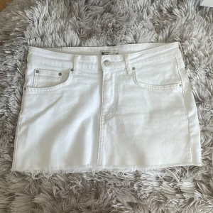 Vit jeanskjol från Gina Tricot - Vit kort jeanskjol från Gina med klassisk femficksdesign, rå kant nertill och bälteshällor. Snygg och enkel modell som passar till allt, perfekt för dig som gillar en clean och fräsch stil. Säljer då den är för stor för mig.