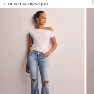 Bootcut ljusblå jeans med slitningar - Bootcut jeans i ljusblå tvätt med slitna detaljer över knäna. Hög midja och klassisk femficksmodell med extra ficklock bak. Jeansen har dragkedjegylf och är tillverkade i mjukt denimtyg. Perfekta för en avslappnad och trendig look. Använda max 2-3 ggr och säljer då dem är för stora för mig.