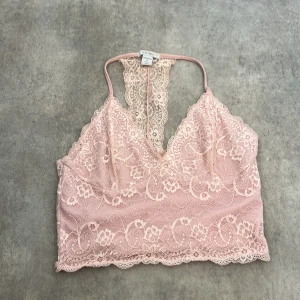Rosa spets bralette från Amisu - Supersöt ljusrosa bralette från Amisu med tunna axelband och vacker spets över hela toppen. Blommigt spetsmönster och snygg racerback-detalj i ryggen. Perfekt att styla under en öppen skjorta eller till höga jeans.
