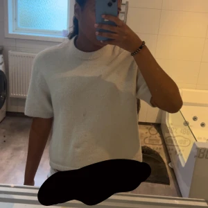 Vit stickad kortärmad tröja - Mysig vit stickad tröja med korta ärmar och rund hals. Perfekt för lager-på-lager och enkel att matcha med olika stilar. Tröjan har en relaxed fit och ribbade kanter vid ärmslut och hals.