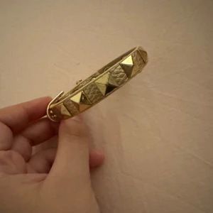 Beige armband med guldnitar - Snyggt armband i beige med guldiga pyramidformade nitar. Köpt på secondhand och använd bara en gång