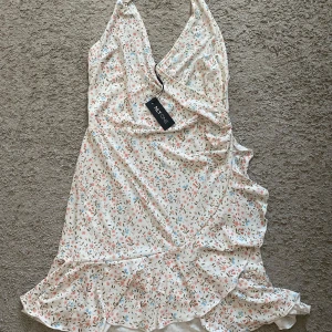 Blommig omlottklänning från NLY One - Supersöt kort omlottklänning från NLY One i vitt med små blommor i rosa, blått och grönt. Klänningen har volangdetaljer, v-ringning och är ärmlös. Perfekt för sommarens alla tillfällen!