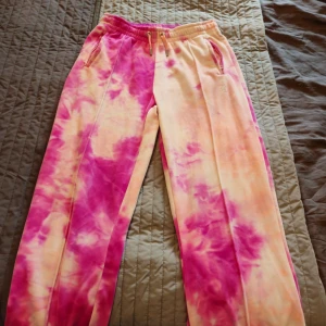Juicy Couture tie dye mjukisbyxor S - Supermjuka mjukisbyxor från Juicy Couture i rosa och tie dye. Byxorna har resår och snörning i midjan, dragkedjeförsedda fickor och glittrig JC-logga framtill. Även det klassiska 'juicy' över rumpan. Perfekta för chill eller streetstyle.