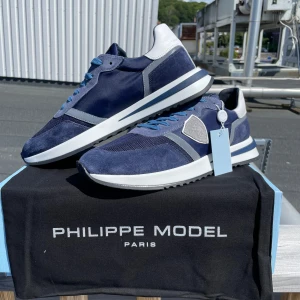 Blå sneakers Philippe Model Tropez - Snygga sneakers från Philippe Model i marinblå mocka och mesh med vita och grå detaljer. Skorna har rund tå, platt sula och blå snörning. Perfekt för dig som gillar stilrena och sportiga skor med exklusiv känsla.