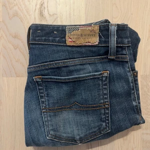  Denim & Supply Ralph Lauren Jeans - Snygga blå jeans från Denim & Supply Ralph Lauren med klassisk femficksdesign och slitna detaljer. Jeansen har en smal passform och är tillverkade i mjukt denimtyg med orange kontrastsömmar. Perfekta för en avslappnad och cool look. Längd 101 midja 38-40 benöppning 14 inseam 80