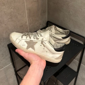 Golden Goose Superstar - Tja! Säljer dessa riktigt feta vita/gråa Golden Goose skor utav modellen ”Superstar”. Skorna är i helt ok skick, de är design att de ska se lite slitna ut! De har hål i sulan som de flesta golden goose får, men de går nog att fixa hos skomakaren ganska billigt. Size 41. Skriv vid funderingar!