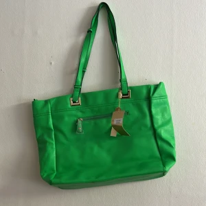 Grön axelväska från H&C - Snygg grön axelväska från H&C med guldiga metalldetaljer och justerbara axelband. Väskan har en praktisk ytterficka med dragkedja och är tillverkad i slätt syntetmaterial. Perfekt för dig som vill sticka ut med en färgstark accessoar.