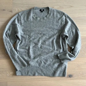 Grå stickad tröja från Uniqlo - En stilren grå stickad tröja från Uniqlo i klassisk modell med rund halsringning och ribbade muddar. Perfekt för lager-på-lager och funkar till allt. Mjuk och skön känsla, passar dig som gillar enkel och clean stil. 100% kashmir