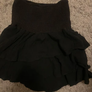 Svart volangkjol från SHEIN - Supersöt svart kortkjol från SHEIN med bred smock i midjan och flera lager volanger. Kjolen är enkel att matcha och har en feminin vibe med sin volangkant. Perfekt för dig som gillar en trendig och lekfull stil.