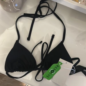 Svart triangelbikini - Svart vadderad triangel bikiniöverdel från NA-KD med smala knytband i nacken och ryggen. Tillverkad i återvunnen polyester (Repreve). Enkel och stilren modell som är perfekt för stranden. Helt oanvänd med prislapp kvar! Slker pga för liten😚