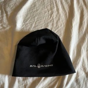 Svart mössa från Sail Racing - Svart mössa från Sail Racing med stilren logga framtill. Enkel och clean design som passar perfekt till kalla dagar. Tillverkad i mjukt syntetmaterial som sitter skönt på huvudet.