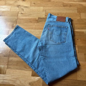 Levi's 501 ljusblå jeans  - Klassiska Levi's 501 jeans i ljusblå denim. Rak passform med normal midja. Klassisk Levi’s märke bak i midjan och röd Levi's-tagg på bakfickan. Perfekta för en avslappnad och tidlös stil.