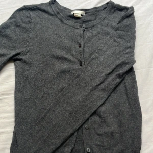Mörkgrå kofta från H&M XS - Mysig mörkgrå kofta från H&M i storlek XS. Den har rund halsringning, långa ärmar och knäppning framtill med små knappar. Materialet är mjukt och stickat, perfekt att slänga på sig över en t-shirt eller linne.