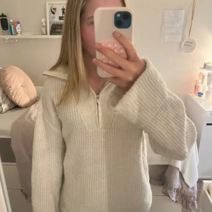 Vit stickad tröja med half zip - Mysig vit stickad tröja med bred krage och half zip-dragkedja framtill. Tröjan har långa ärmar och en loose passform som ger en chill vibe. Perfekt för lager på lager under höst och vinter. Enkel att matcha med jeans eller leggings.